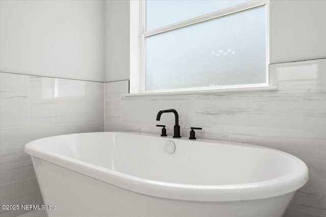 bathroom featuring a wealth of natural light, a freestanding bath, and tile walls