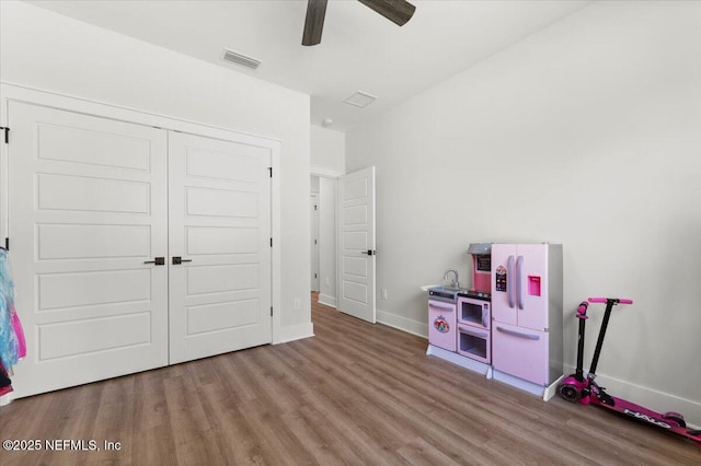 recreation room with a ceiling fan, wood finished floors, visible vents, and baseboards