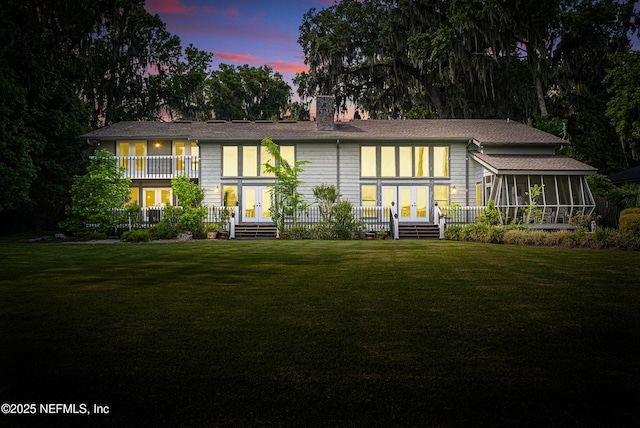view of front of property with a sunroom, french doors, a lawn, and a chimney