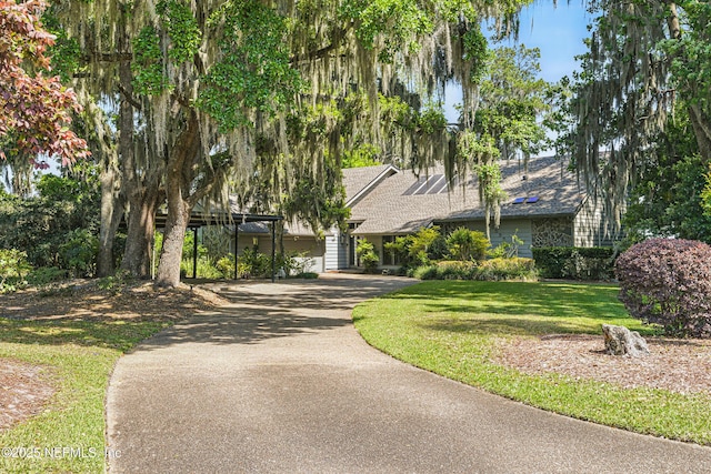 view of property hidden behind natural elements with aphalt driveway, a shingled roof, and a front lawn
