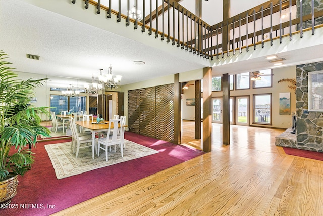 dining space with a high ceiling, ceiling fan with notable chandelier, visible vents, and wood finished floors