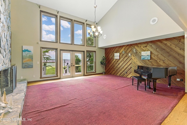 living area with a notable chandelier, a stone fireplace, wooden walls, french doors, and high vaulted ceiling