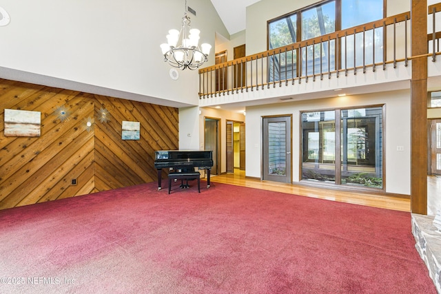 living room featuring wood walls, plenty of natural light, a towering ceiling, and an inviting chandelier