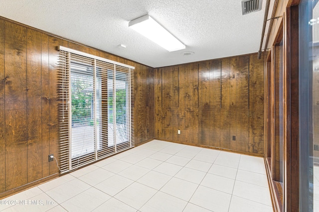 spare room featuring wood walls, visible vents, and a textured ceiling