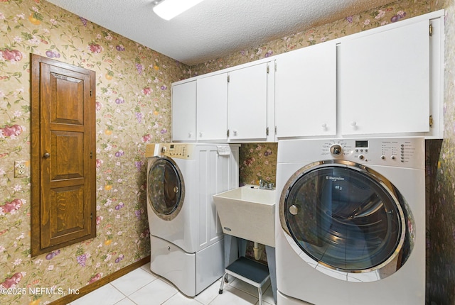 washroom with a textured ceiling, wallpapered walls, cabinet space, and washer and clothes dryer
