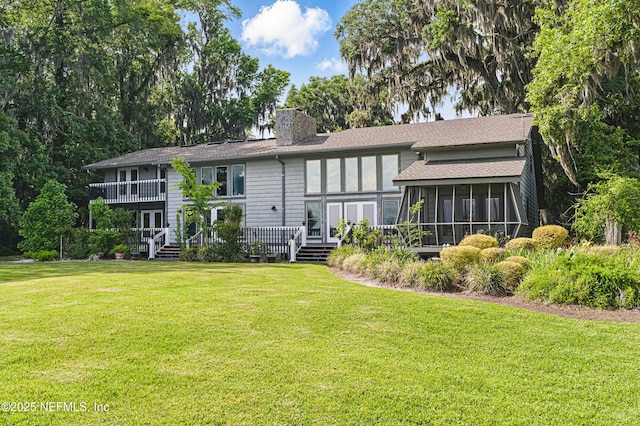 rear view of property featuring a yard, roof with shingles, a sunroom, and a chimney