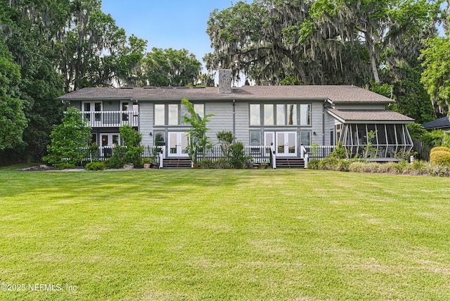 rear view of property with a sunroom, french doors, a lawn, and a chimney