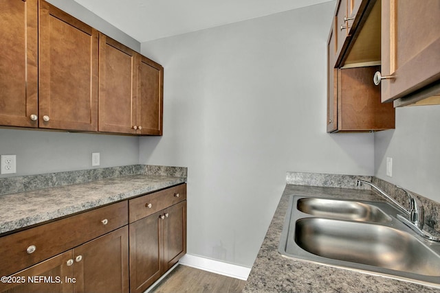 kitchen with wood finished floors, baseboards, a sink, light countertops, and brown cabinets