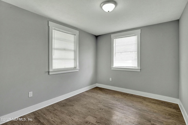 unfurnished room with baseboards, dark wood-type flooring, and a textured ceiling