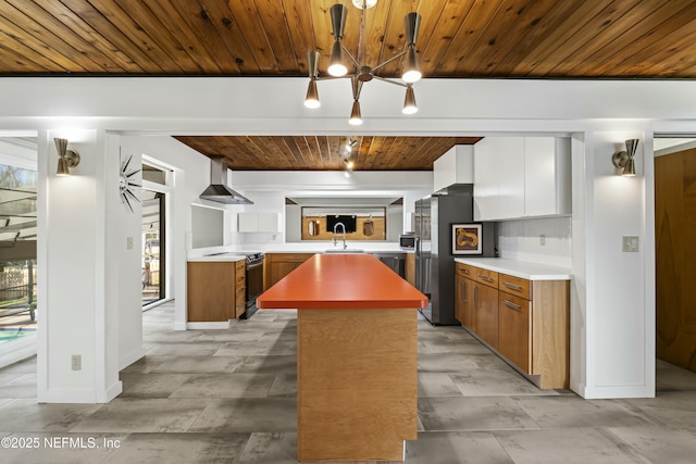 kitchen with a kitchen island, a sink, appliances with stainless steel finishes, wall chimney exhaust hood, and brown cabinets