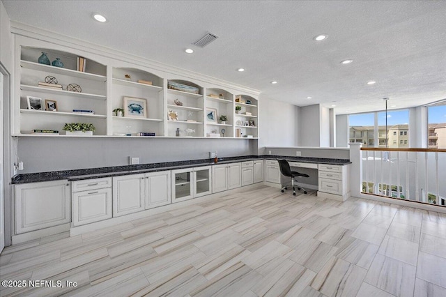 unfurnished office with visible vents, a textured ceiling, floor to ceiling windows, built in desk, and recessed lighting