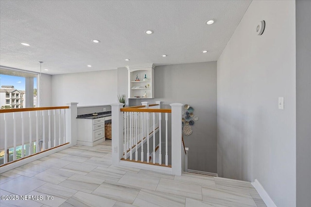 hallway with an upstairs landing, recessed lighting, a textured ceiling, and baseboards