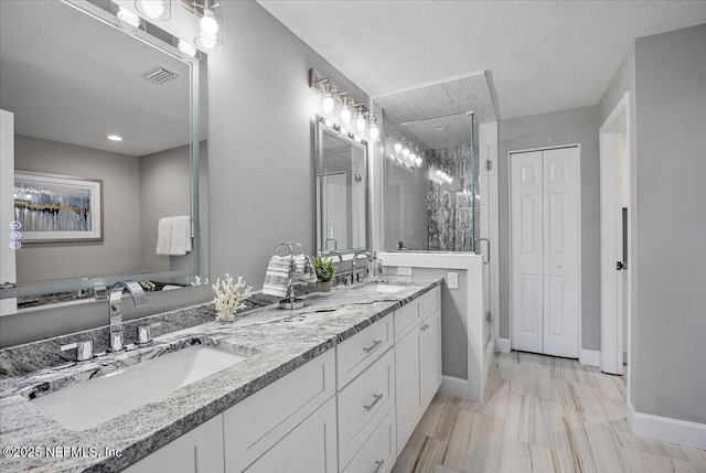 bathroom with a textured ceiling, double vanity, a stall shower, and a sink