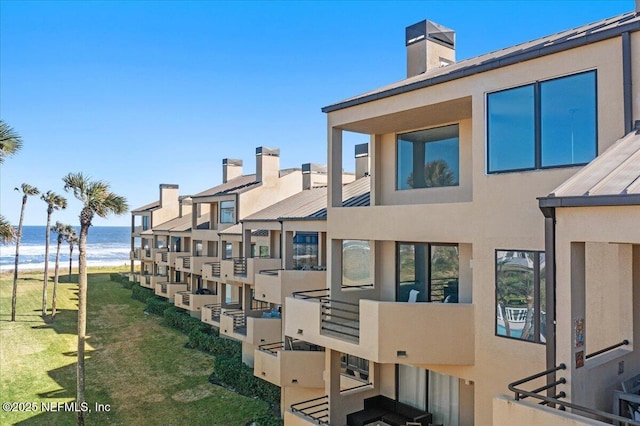 exterior space featuring a water view, stucco siding, metal roof, a chimney, and a standing seam roof