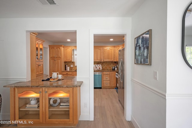 kitchen with light wood finished floors, visible vents, dark stone counters, decorative backsplash, and stainless steel dishwasher