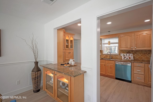 kitchen with dishwashing machine, dark stone countertops, light wood-type flooring, a sink, and tasteful backsplash