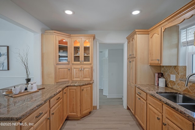 kitchen featuring tasteful backsplash, dark stone countertops, light wood-type flooring, and a sink