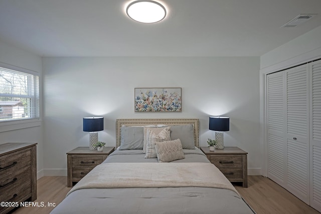 bedroom featuring light wood-type flooring, visible vents, baseboards, and a closet