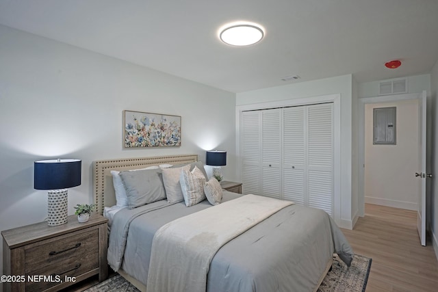 bedroom with electric panel, visible vents, light wood-type flooring, and a closet