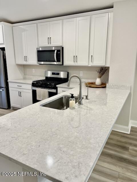 kitchen with white cabinets, stainless steel appliances, light wood-style flooring, and a sink