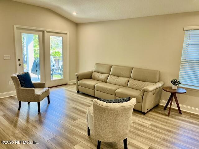 living room featuring light wood-type flooring, baseboards, and lofted ceiling