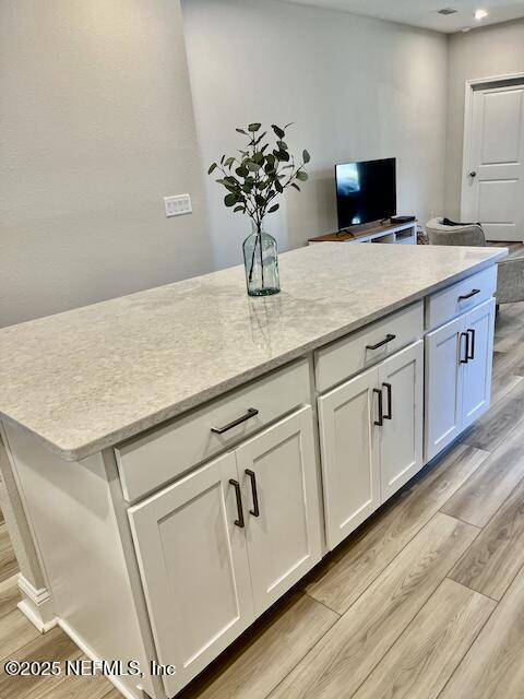 kitchen with white cabinetry, light stone countertops, light wood finished floors, and a kitchen island