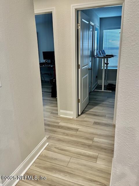 corridor featuring baseboards, wood tiled floor, and a textured wall