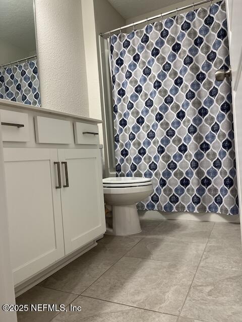 bathroom with curtained shower, toilet, tile patterned flooring, and a textured wall