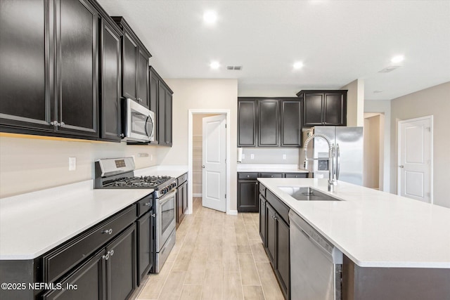 kitchen with visible vents, an island with sink, stainless steel appliances, light wood-style floors, and light countertops