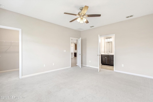 unfurnished bedroom featuring visible vents, baseboards, ensuite bath, a walk in closet, and light colored carpet