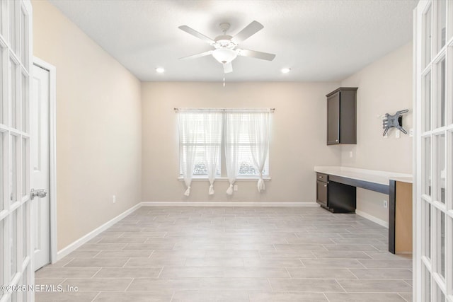 interior space featuring french doors, a ceiling fan, baseboards, and built in desk