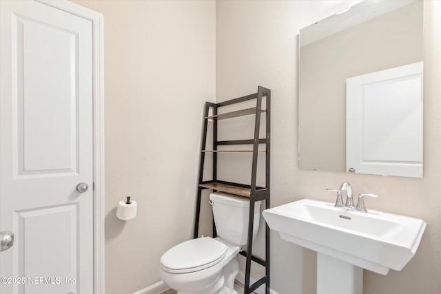 half bathroom with toilet, baseboards, and a sink