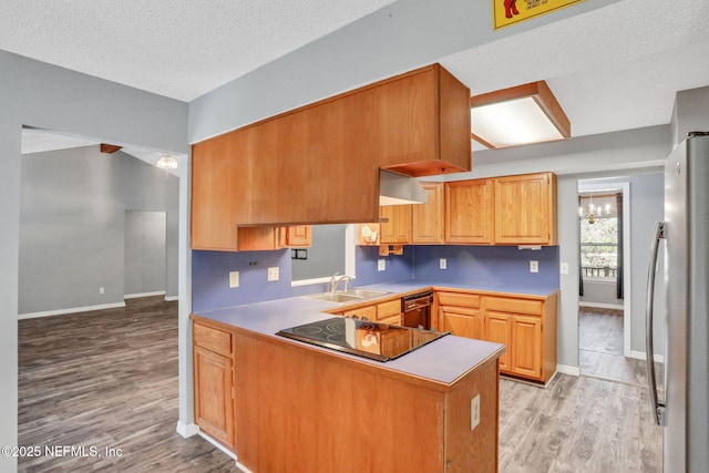 kitchen with black appliances, a peninsula, light wood-type flooring, and a sink