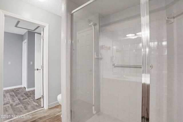 bathroom featuring toilet, a textured ceiling, wood finished floors, a shower stall, and baseboards