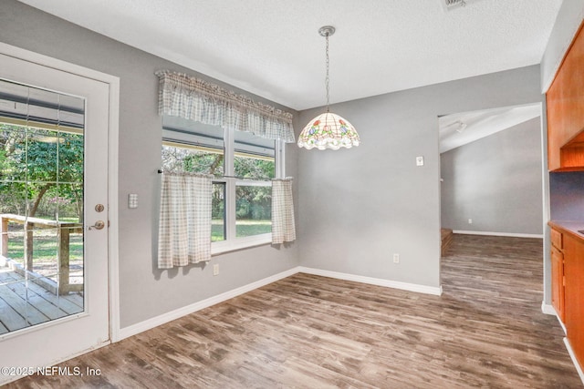 unfurnished dining area with baseboards, a textured ceiling, and wood finished floors