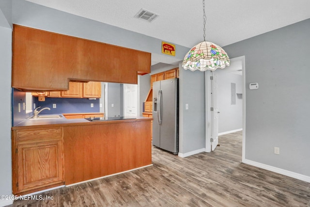 kitchen featuring stainless steel refrigerator with ice dispenser, a sink, wood finished floors, a peninsula, and black electric stovetop