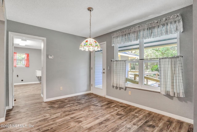 unfurnished dining area with a textured ceiling, baseboards, and wood finished floors