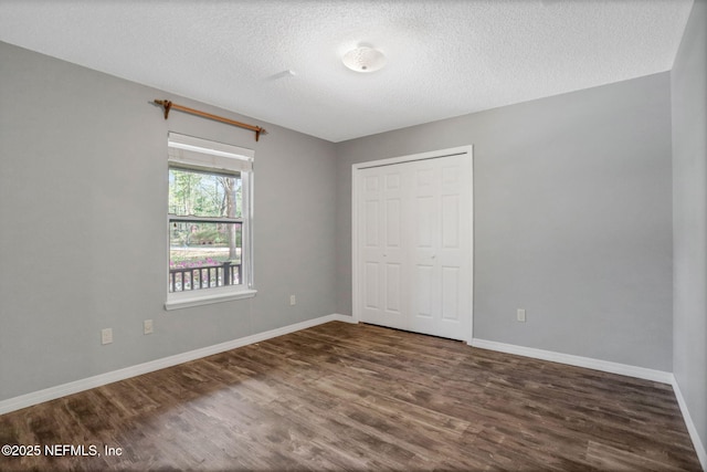 unfurnished bedroom with a closet, baseboards, a textured ceiling, and dark wood finished floors