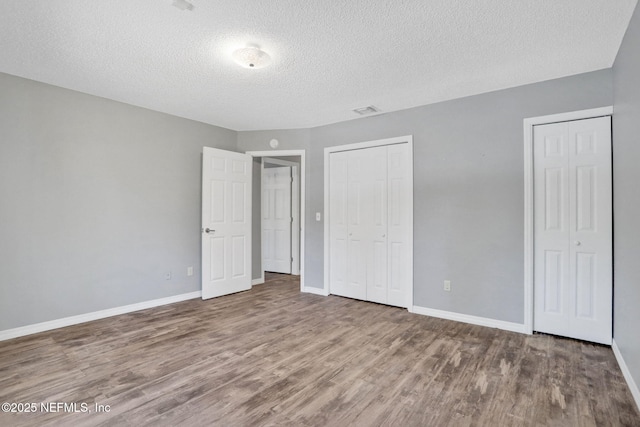 unfurnished bedroom featuring visible vents, two closets, a textured ceiling, wood finished floors, and baseboards