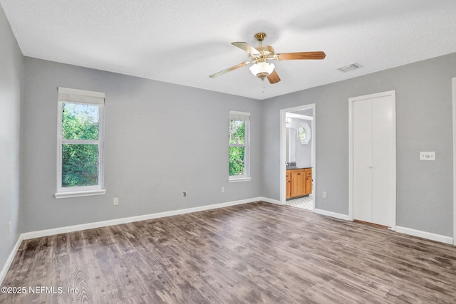 unfurnished bedroom featuring visible vents, a textured ceiling, baseboards, and wood finished floors