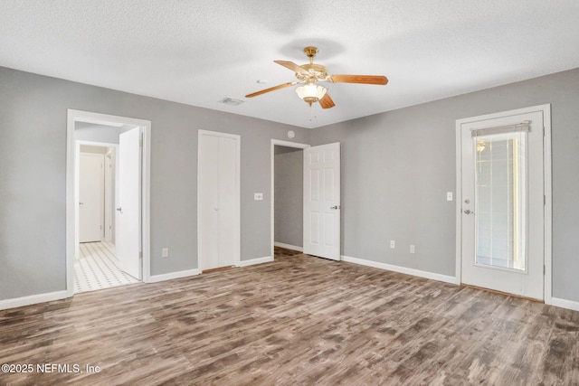 unfurnished bedroom featuring visible vents, baseboards, wood finished floors, a textured ceiling, and ensuite bath