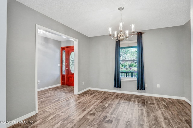 empty room with baseboards, wood finished floors, a textured ceiling, and a chandelier