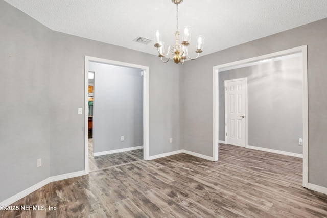 spare room with visible vents, baseboards, an inviting chandelier, and wood finished floors