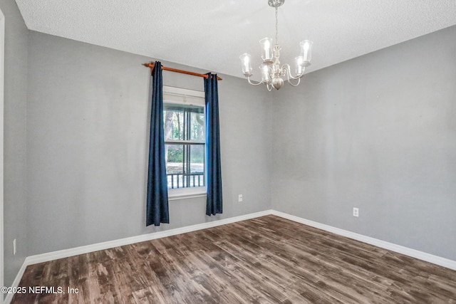 empty room with dark wood-style floors, baseboards, a textured ceiling, and a chandelier