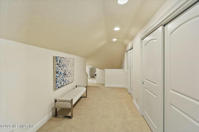 hall featuring vaulted ceiling, light carpet, baseboards, and a textured ceiling