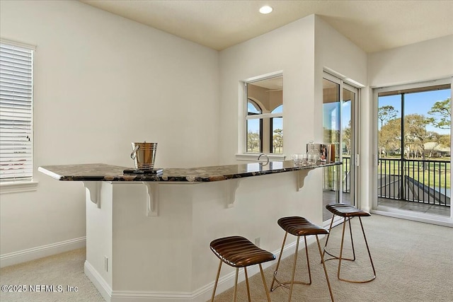 kitchen with baseboards, light colored carpet, dark stone counters, a kitchen bar, and recessed lighting