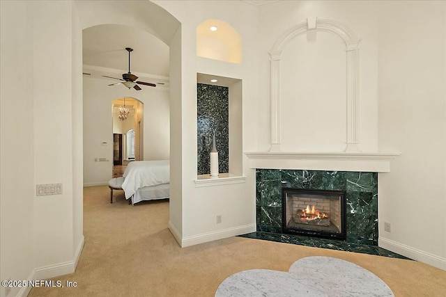 interior space featuring ceiling fan, baseboards, carpet, a premium fireplace, and arched walkways