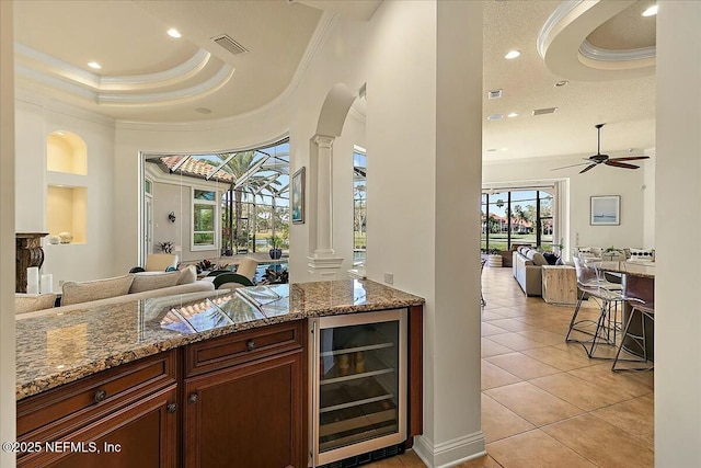 bar featuring beverage cooler, visible vents, decorative columns, crown molding, and a raised ceiling