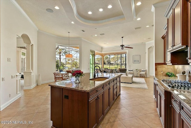 kitchen with a sink, open floor plan, stainless steel gas stovetop, decorative columns, and ceiling fan