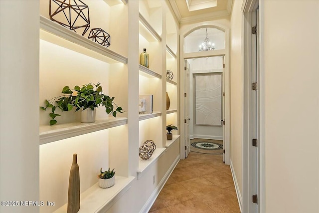 hallway with tile patterned floors, built in features, an inviting chandelier, crown molding, and baseboards